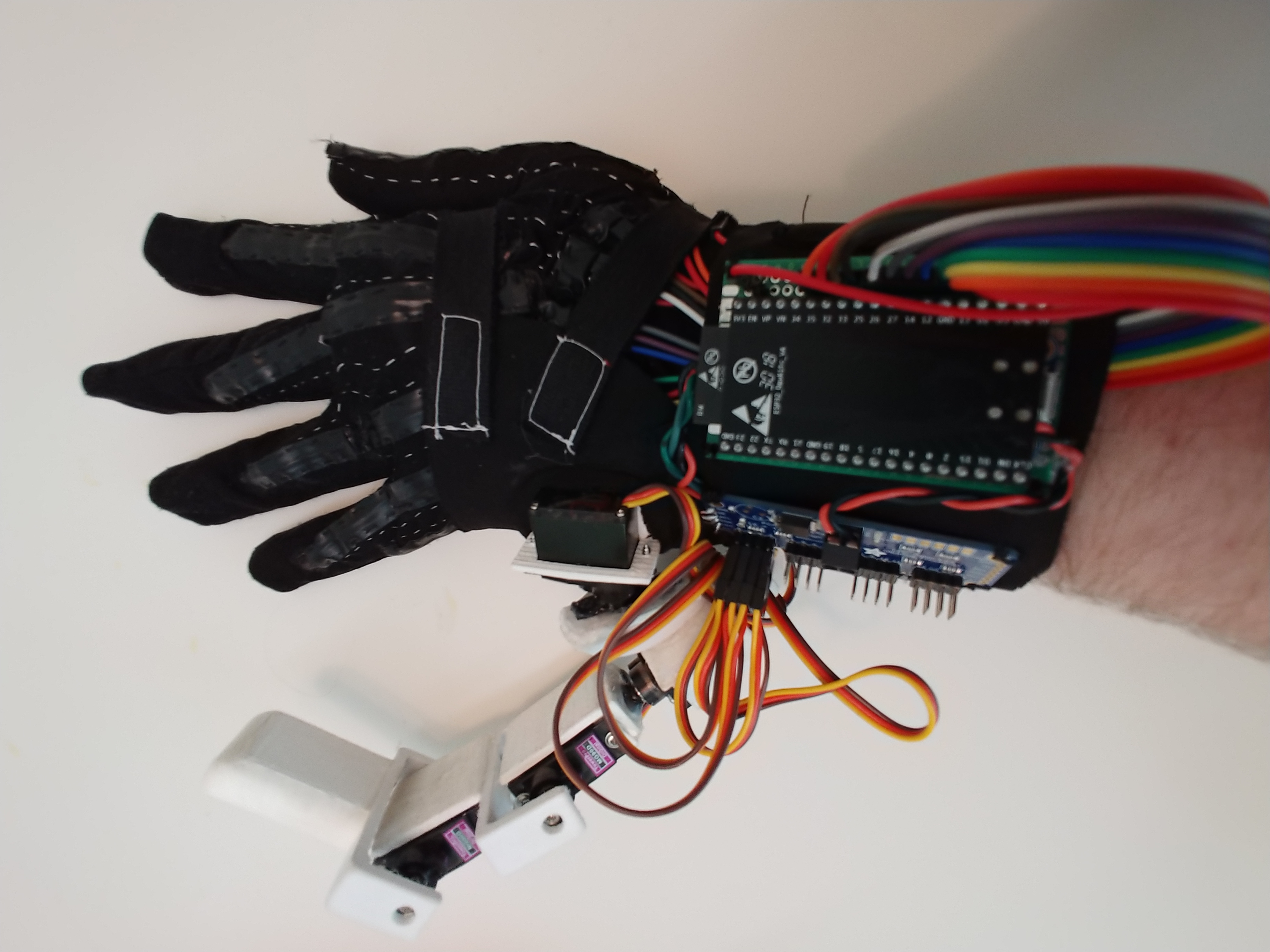 Picture shows a gloved hand with the robotic finger attached. Control board (ESP32) is also shown.