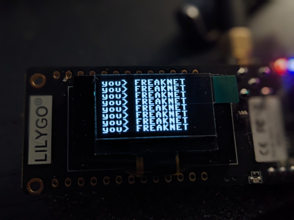 A photo of a LYLIGO TTGO LoRa v2 1.6 showing the text: you> FREAKNET in multiple lines.