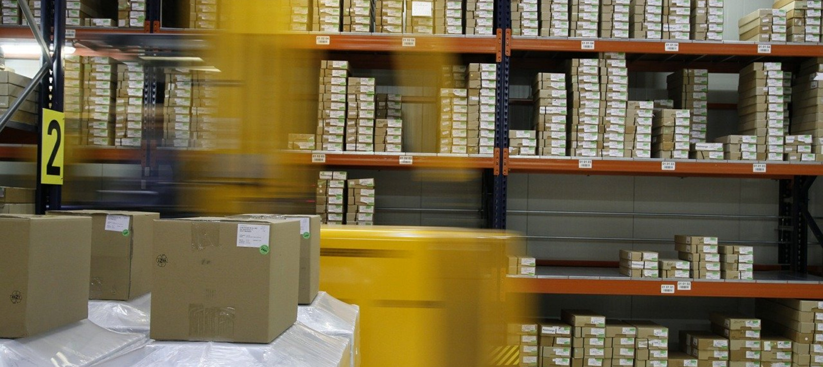 A photo of a blurry fork lift driving through a warehouse with lots of items on the shelves.